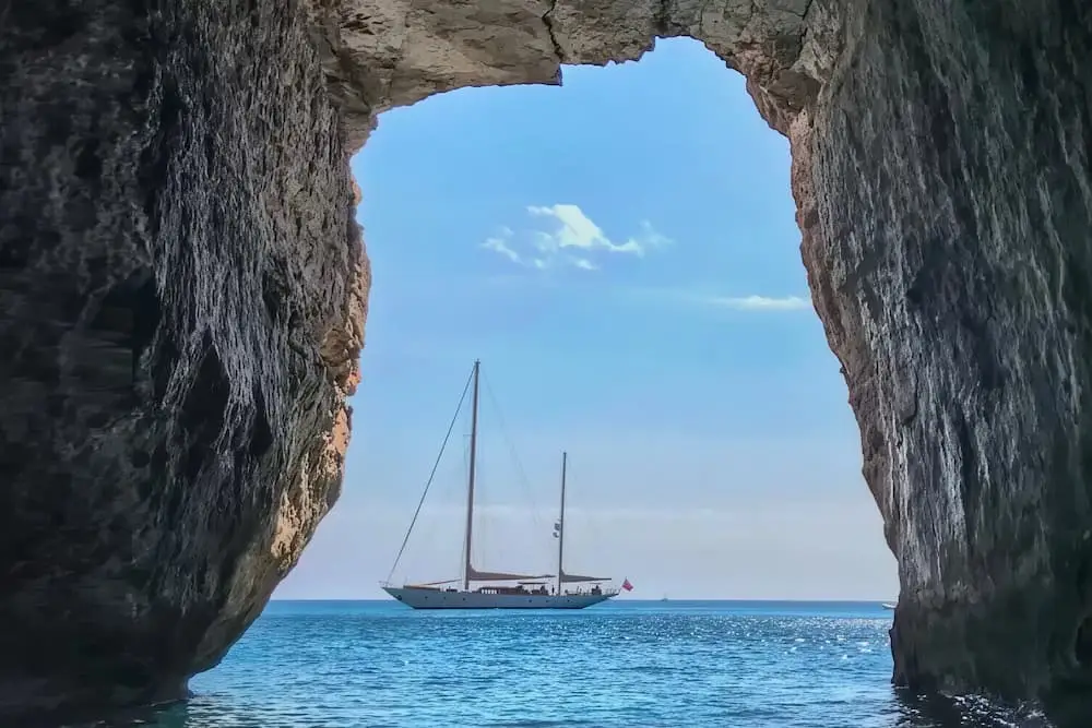 Velero enmarcado por la Cueva de la Ventana en la ruta de kayak en Es Canutells, Menorca